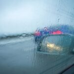 Zamglona szyba auta w deszczu z rozmytymi światłami samochodów na drodze