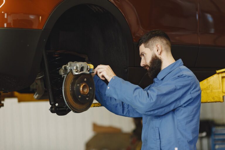 Mechanik w niebieskim kombinezonie naprawiający hamulce samochodu w warsztacie